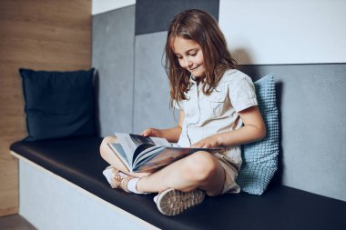 Okul kütüphanesinde kitap okuyan liseli kız. İlkokul öğrencisi kitapla ilgileniyor. Ödev yapan çocuk. Akıllı kız kitaptan öğreniyor. Günlük okumanın faydaları. Çocuk merakı