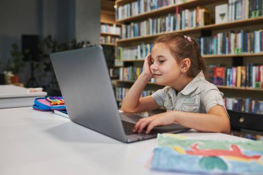 Positively engaged student doing her homework using laptop in after school club at primary school. Back to school. Child using technology on elementary computer science class. Smart little girl learning from educational application at school. Child s