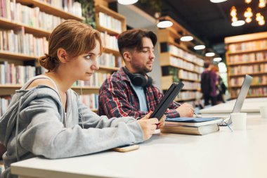 Students learning in university library. Young man preparing for test on laptop. Girl writing essay and making notes using computer. Focused students studying for college exams. Students discussing and learning together sitting at desk. Back to schoo