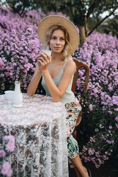 Jovem Loira Sentada Mesa Com Xícara Chá Jardim Flores Mon — Fotografia de Stock