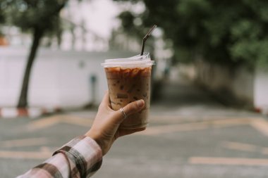 Arka planda bulanık kahve ile plastik bardak tutan bir kadın.