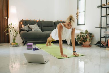 Sarışın bir kadın yerde oturuyor ve internette eğitim görüyor. Bilgisayara bakıyor..