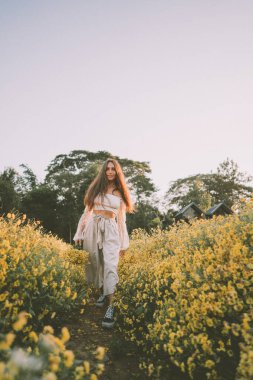 Genç ve çekici bir kadın Chiang Mai 'deki sarı çiçek tarlasında eğleniyor.