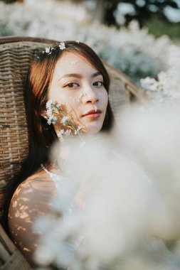Portrait of thai woman sitting in a straw chair in flower field
