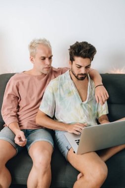 Gay couple sitting on sofa with laptop in their house