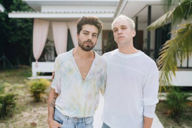 Gay hugging couple standing in front of their house outdoors