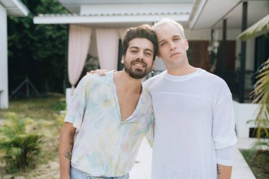 Gay hugging couple standing in front of their house outdoors
