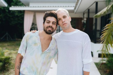 Gay hugging couple standing in front of their house outdoors