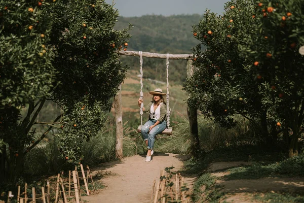 Thai woman in casual style is sitting on swing in an orange garden — 스톡 사진
