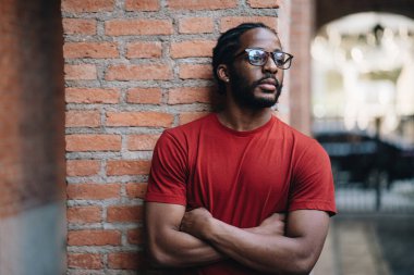 Kırmızı tişörtlü ve gözlüklü siyahi bir adamın portresi.