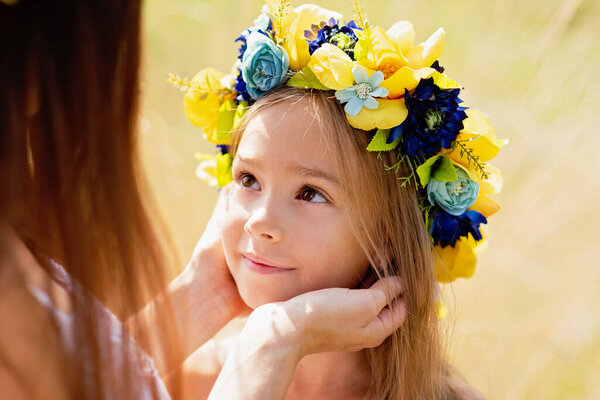 mother and daughter in traditional Ukrainian wreaths in on head blue and yellow flag of Ukraine in field. Ukraine Independence Flag Day. Constitution day. 24 August. Patriotic holiday. Woman and child