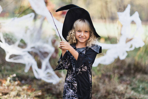 Beautiful girl witch. little girl in whitch costume and hat celebrate Halloween outdoor and have fun. Kids trick or treating. girl witch with magic Book of spells, broom