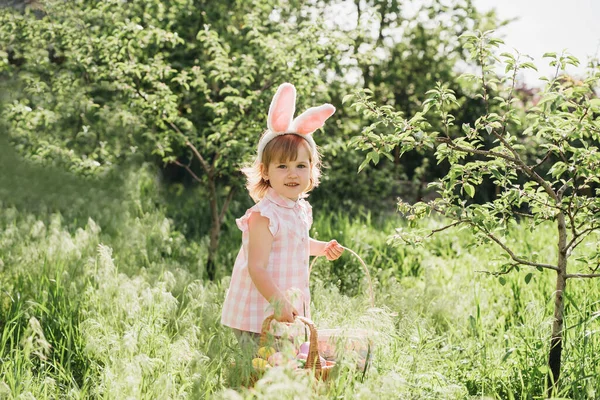 イースターエッグハント 庭で卵を拾うために実行しているバニーの耳を身に着けている女の子の子供 イースターの伝統 カラフルな卵がいっぱい入ったバスケットの赤ちゃん 広角ビュー — ストック写真