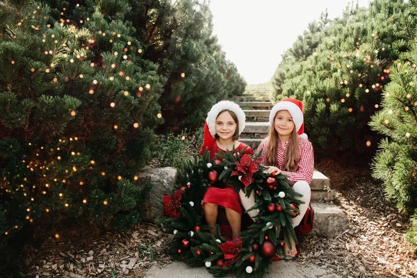 メリークリスマス クリスマスリースとサンタの帽子の2つの幸せな面白い子供たちの女の子の肖像画 ハッピー ホリデー 妖精の魔法 休日を楽しんでいる幸せな子供たち 7月のクリスマス — ストック写真