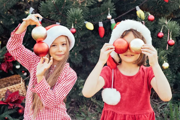 メリークリスマス。肖像画の二つの幸せな面白い子供たちの女の子でサンタ帽子とともにクリスマス花輪 — ストック写真