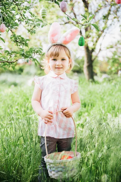 Baby with basket full of colorful eggs. Easter egg hunt. — Stock Photo, Image