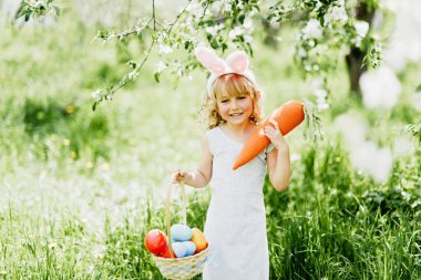 Cute funny girl with Easter eggs and bunny ears at garden. Easter concept.