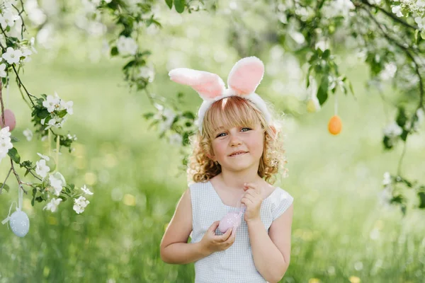 Gadis lucu dengan telur Paskah dan telinga kelinci di taman. konsep easter. Tertawa anak di Paskah berburu telur — Stok Foto