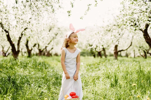 Cute funny girl with Easter eggs and bunny ears at garden. easter concept. Laughing child at Easter egg hunt — Stock Photo, Image