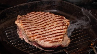 Bifteğin yakın plan eti fırında ızgara demir tırtıklı tavada kızartılıyor..