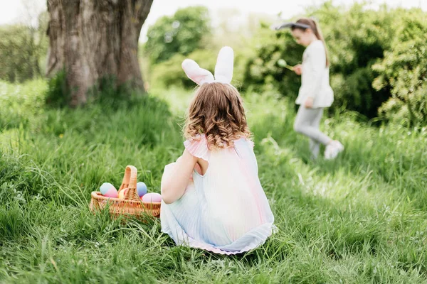 กลุ่มเด็กสวมหูกระต่ายวิ่งไปรับไข่ที่มีสีสันเมื่อล่าไข่อีสเตอร์ในสวน . — ภาพถ่ายสต็อก
