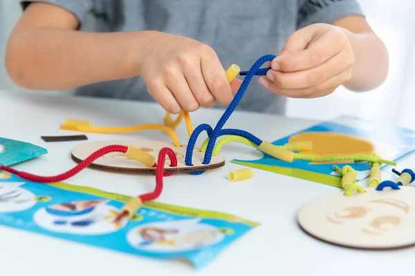 Nahaufnahme von Kinderhänden, die mit Spitze oder Seil und Nudeln spielen. Entwicklung der Feinmotorik. Frühe Bildung, Montessori-Methode. Kognitive Fähigkeiten, — Stockfoto