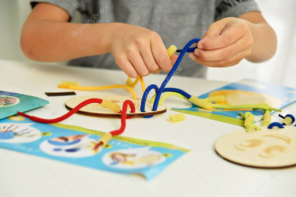 Close up of child hands playing with lace or rope and pasta. development of fine motor skills. Early education, Montessori Method. Cognitive skills,