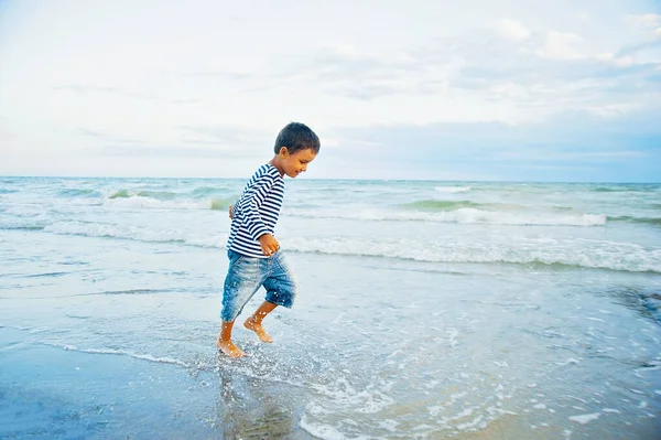 日没時に海のビーチで水上を走る子供。男の子はビーチランで楽しみ、休暇でジャンプします. — ストック写真