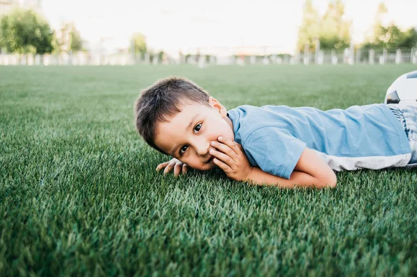 Portrét šťastného chlapce ležícího na fotbalovém hřišti. — Stock fotografie