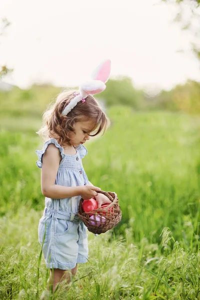 Ребёнок с корзиной, полной разноцветных яиц. Охота на пасхальные яйца. — стоковое фото