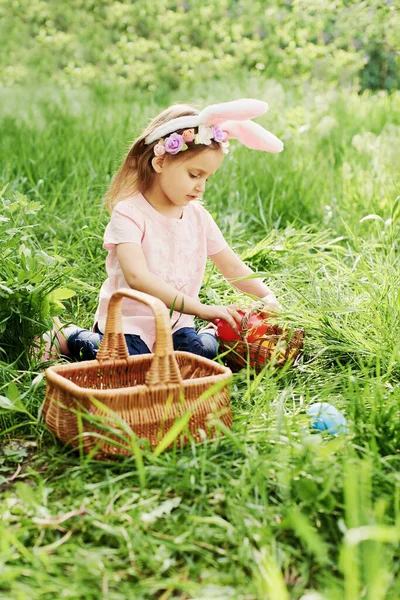 Ребёнок с корзиной, полной разноцветных яиц. Охота на пасхальные яйца. — стоковое фото