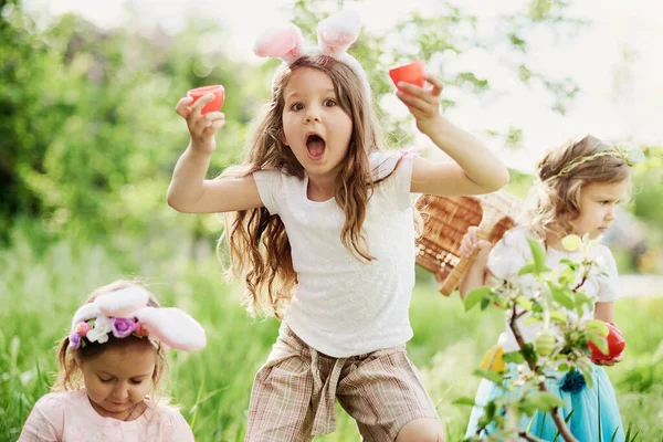 En gruppe barn med kaninører som løper for å plukke opp fargerike egg på påskeeggjakt i hagen. – stockfoto