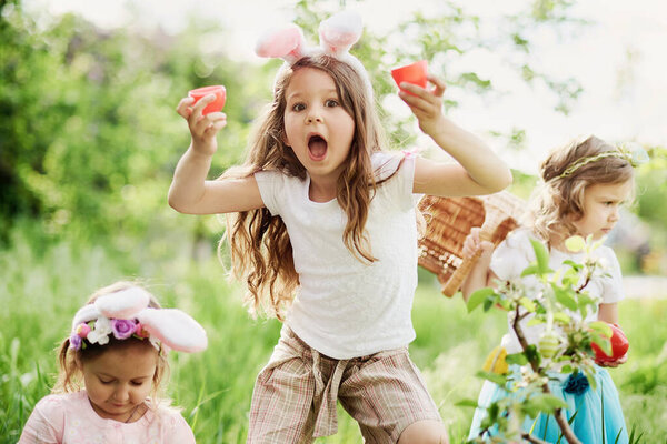 Group Of Children Wearing Bunny Ears Running To Pick Up colorful Egg On Easter Egg Hunt In Garden. Stock Photo
