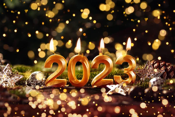 Holiday background Happy New Year 2023. Digits of year 2023 made by burning gold candles on red festive sparkling background.