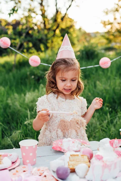 Selamat ulang tahun gadis kecil membuat harapan meniup lilin di kue dengan dekorasi merah muda di taman yang indah — Stok Foto