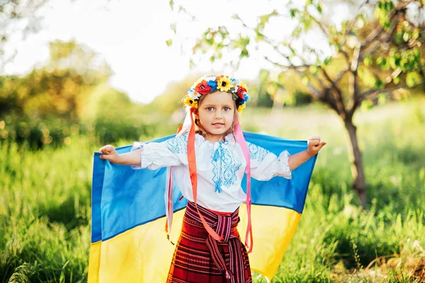 Ukrainian child girl in embroidered shirt vyshyvanka with yellow and blue flag of Ukraine in field. — Stock Photo, Image