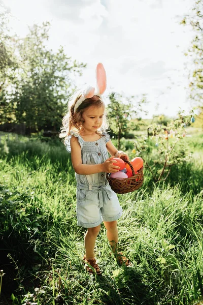 Baby with basket full of colorful eggs. Easter egg hunt. — Stock Photo, Image