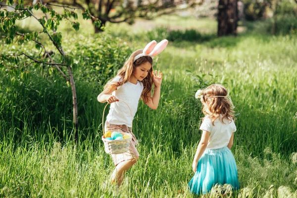 Група дітей, які носять вуха кролика, бігають, щоб підібрати барвисте яйце на Великдень Полювання на яйце в саду. Великодня традиція — стокове фото