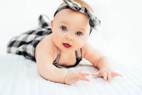 Schattig lachend klein meisje zittend op bed. Zeven maanden oud baby kind op grijze zachte deken — Stockfoto