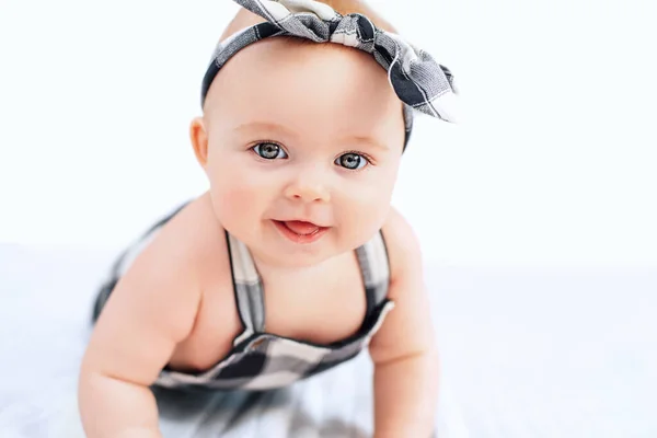 Cute smiling little baby girl sitting on bed. Seven month old infant child on grey soft blanket — Stock Photo, Image