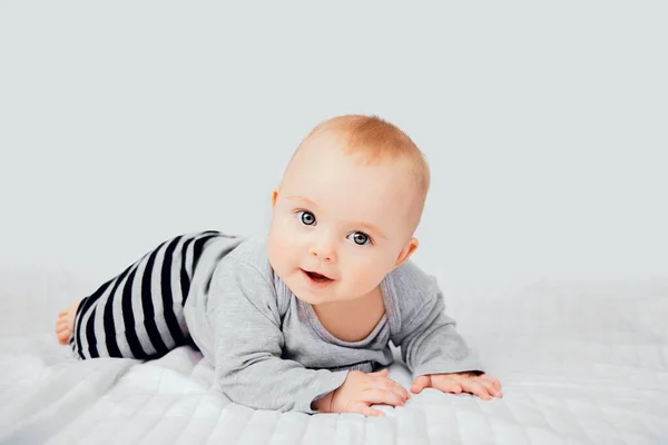 Schattig lachend klein meisje zittend op bed. Zeven maanden oud baby kind op grijze zachte deken — Stockfoto