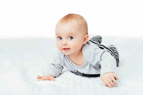 Nettes lächelndes kleines Mädchen, das auf dem Bett sitzt. Sieben Monate altes Säugling auf grauer weicher Decke — Stockfoto