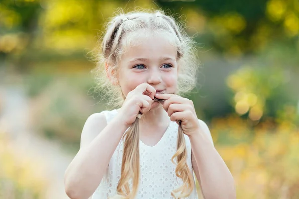 Gadis lucu memegang rambut anyaman. Gadis kecil cantik dengan rambut pirang panjang yang menunjukkan lidah di luar. Anak itu mengekspresikan emosi. April bodoh . — Stok Foto