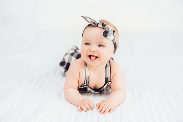 Schattig lachend klein meisje zittend op bed. Zeven maanden oud baby kind op grijze zachte deken — Stockfoto