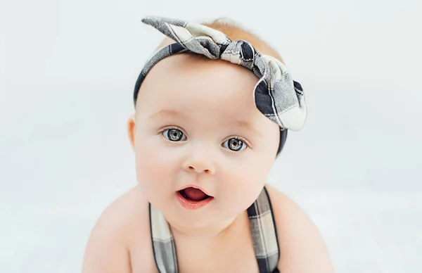 Nettes lächelndes kleines Mädchen, das auf dem Bett sitzt. Sieben Monate altes Säugling auf grauer weicher Decke — Stockfoto