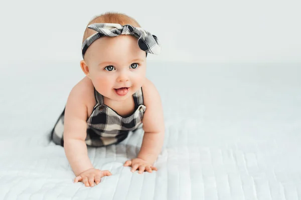 可爱的小女孩坐在床上笑着。7个月大的婴儿躺在灰色柔软的毛毯上 — 图库照片