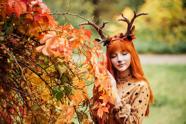 fairy woman with deer horns in autumn forest. Face painting. Beautiful mystery woman. redhead girl with big eyes magical sight