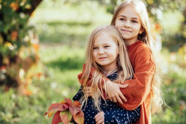 Bahçede sıcak ve güneşli bir yaz gününde birbirine sarılarak gülen iki kız kardeşin portresi. İnsanlar, duygular ve arkadaşlık kavramı. Birlikte eğlenmek, olumlu duygular, parlak renkler..