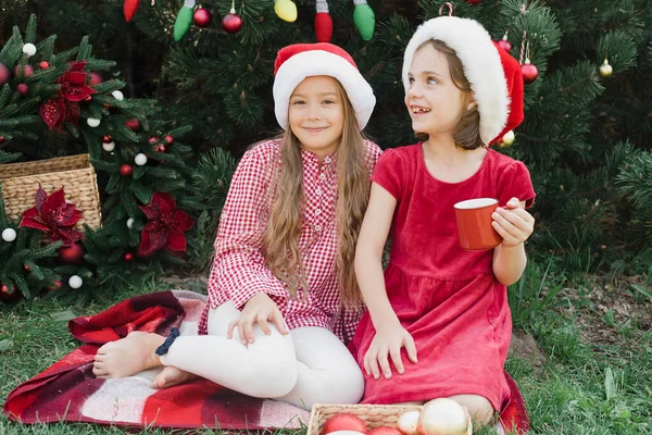 メリークリスマス サンタの帽子の2人の面白い子供の女の子の肖像は 楽しみを持って外ホットチョコレートを飲むジンジャーブレッドクッキーを食べています ハッピー ホリデー 休日を楽しむ子供たち 7月のクリスマス — ストック写真
