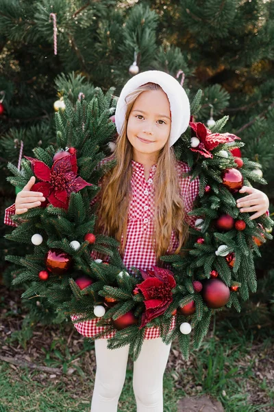 メリークリスマス クリスマスリースとサンタの帽子の幸せな面白い子供の女の子の肖像画 ハッピー ホリデー 妖精の魔法 幸せな子供は休日を楽しんでいる 7月のクリスマス — ストック写真